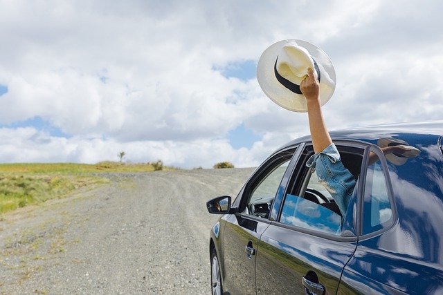 Car driving down highway with window rolled down and a hand holding a hat out the window.